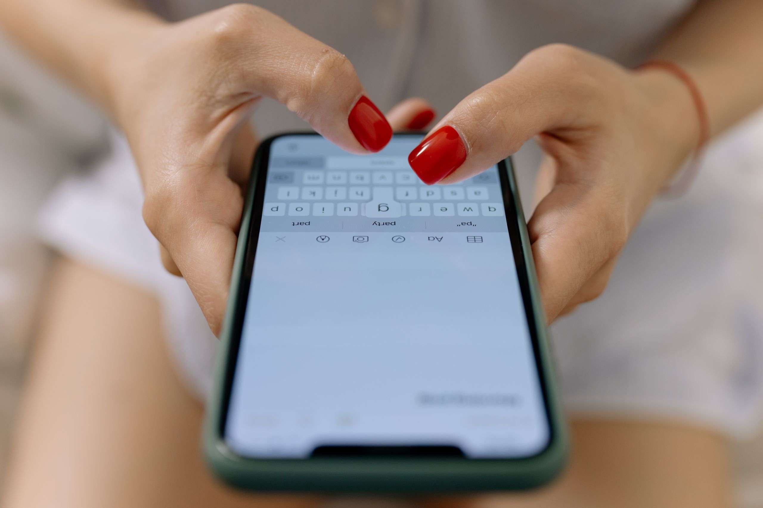 Close-up image of hands with red nails typing on a smartphone screen, showcasing modern technology.