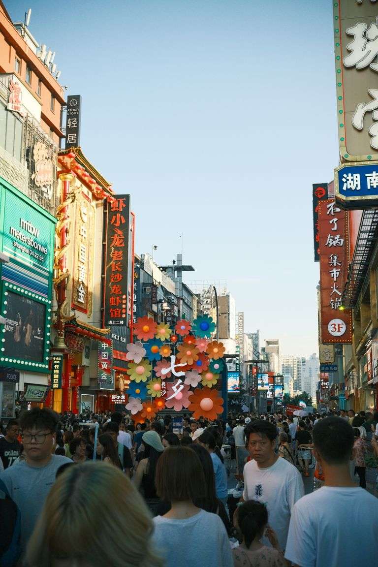 Bustling urban street filled with people and colorful signs in an outdoor market setting.
