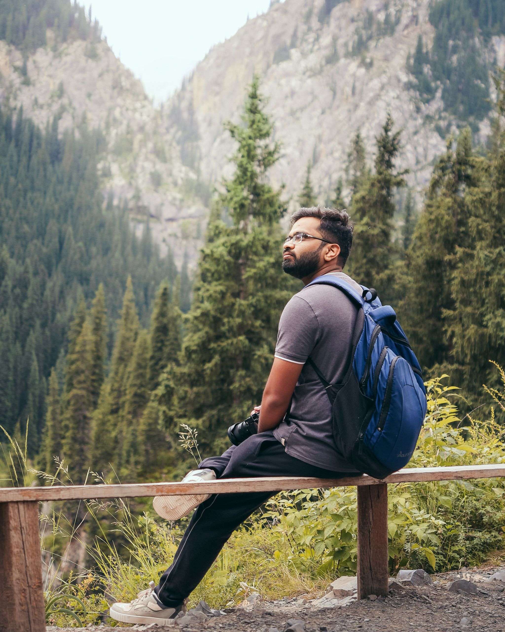 A traveler sits on a wooden bench in the mountains of Kazakhstan, capturing the peaceful essence of solo outdoor adventure.